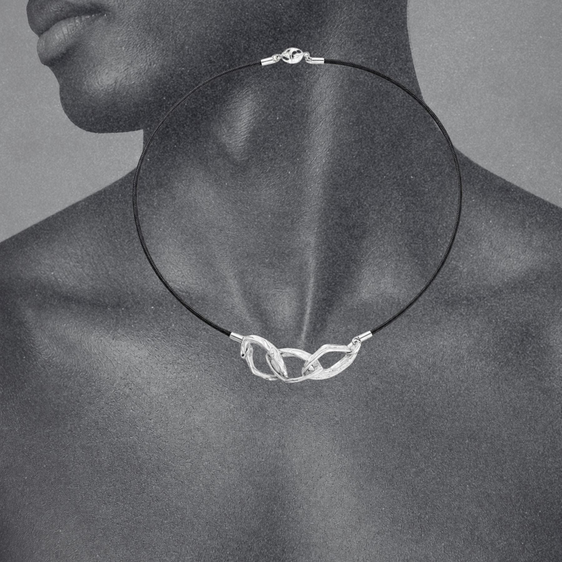 A close-up of a person's neck and upper chest wearing a black silk cord necklace by Jessica Liu with three silver links.