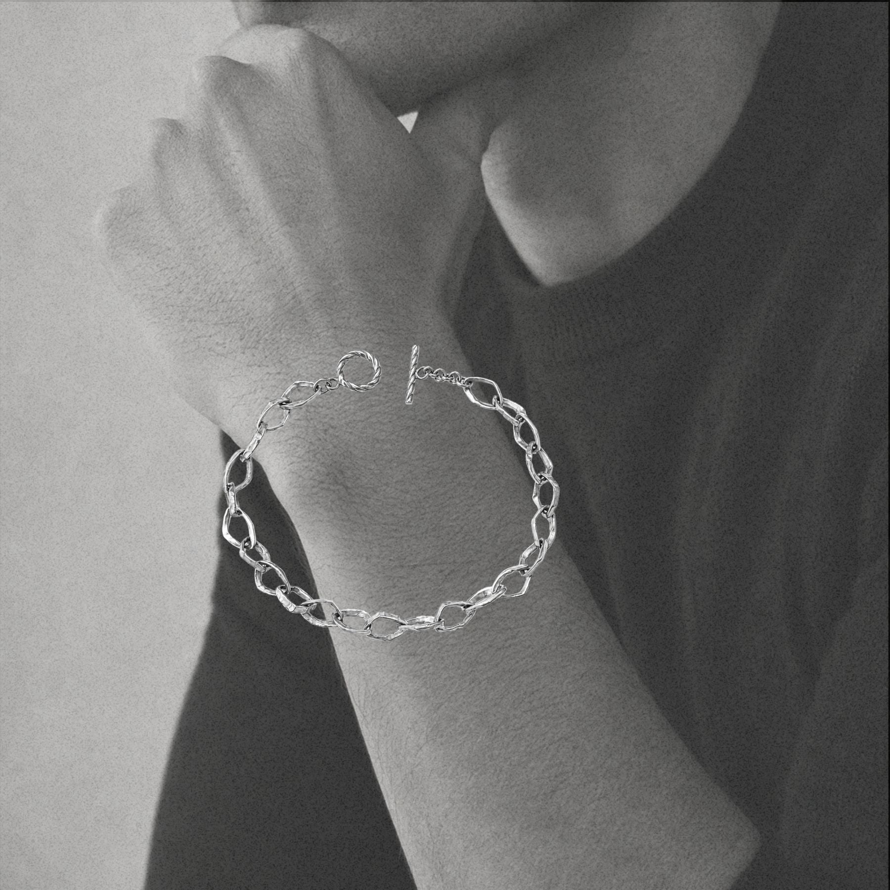 A silver chain bracelet by Jessica Liu with a toggle clasp worn on a person's wrist, shown in a black and white close-up photo.