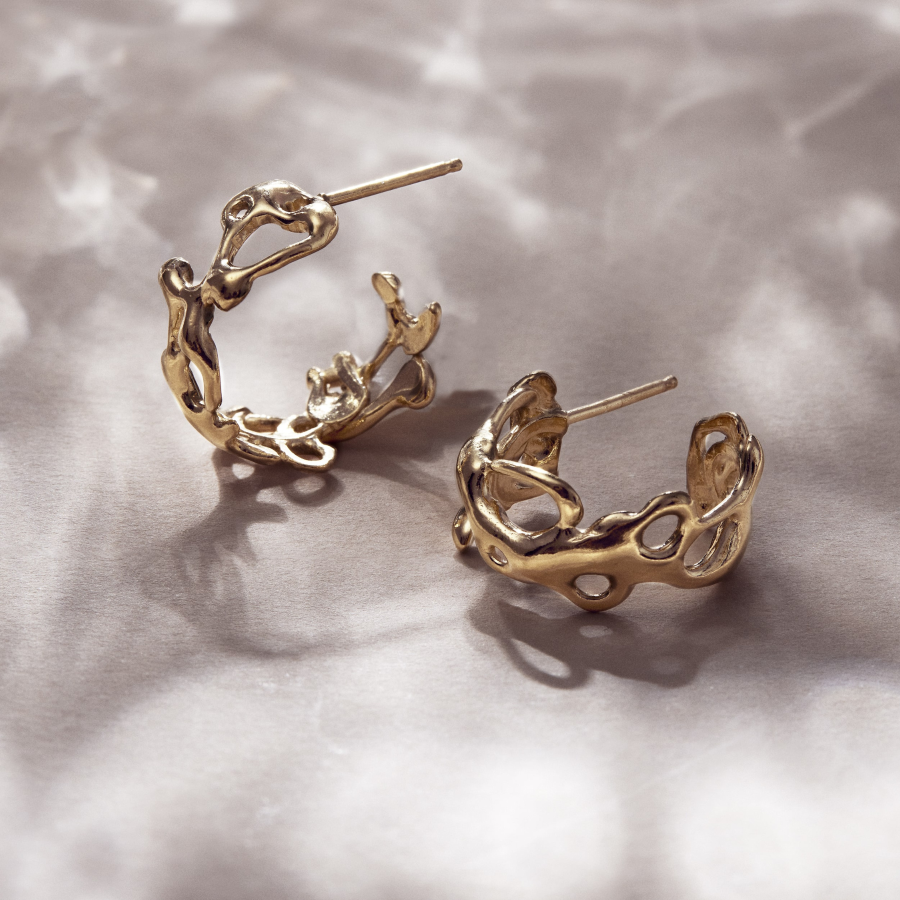 flatlay of 14k gold abstract fluid asymmetrical small hoop earrings by jessica liu