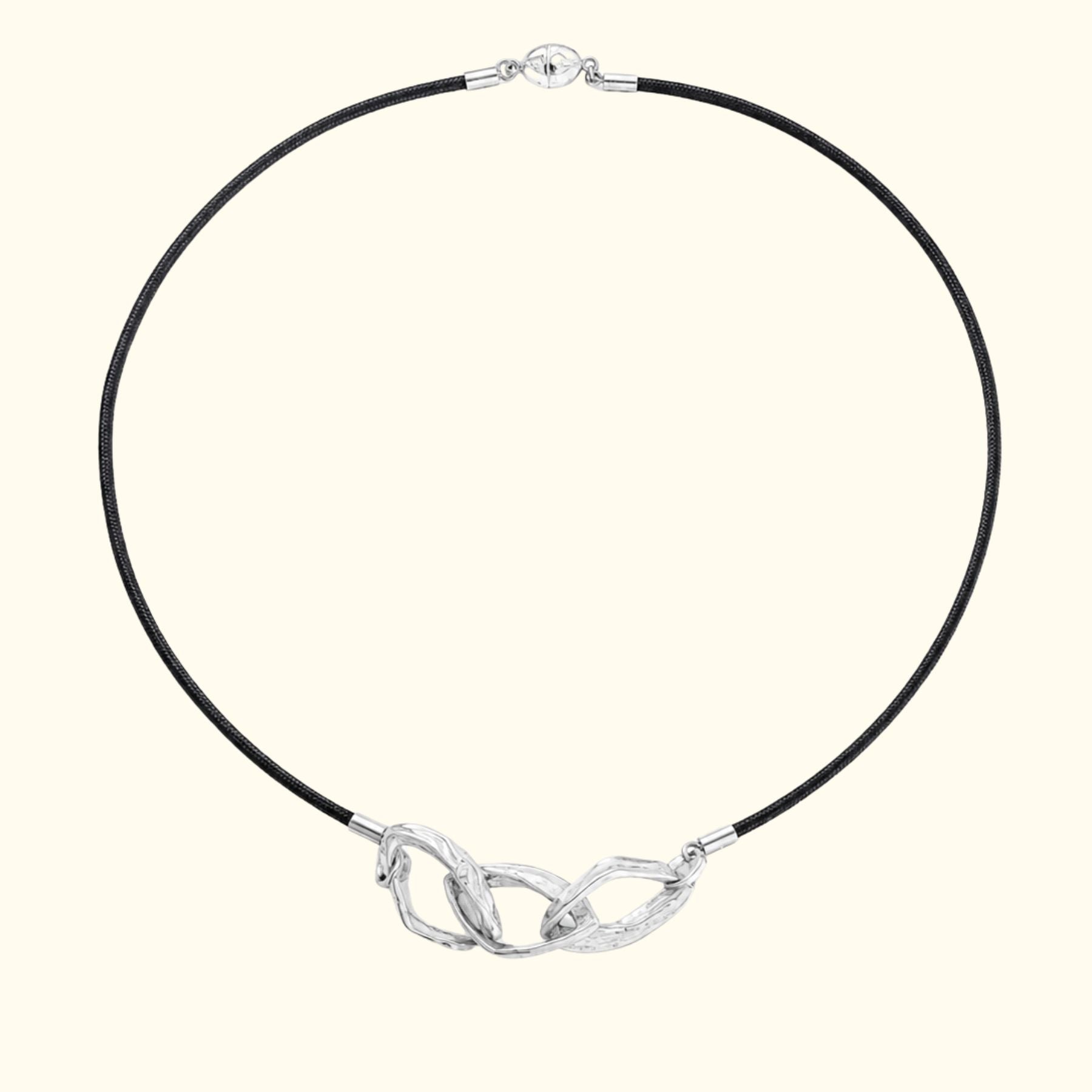 A black silk cord necklace by Jessica Liu with three textured silver links, displayed on a solid cream background.