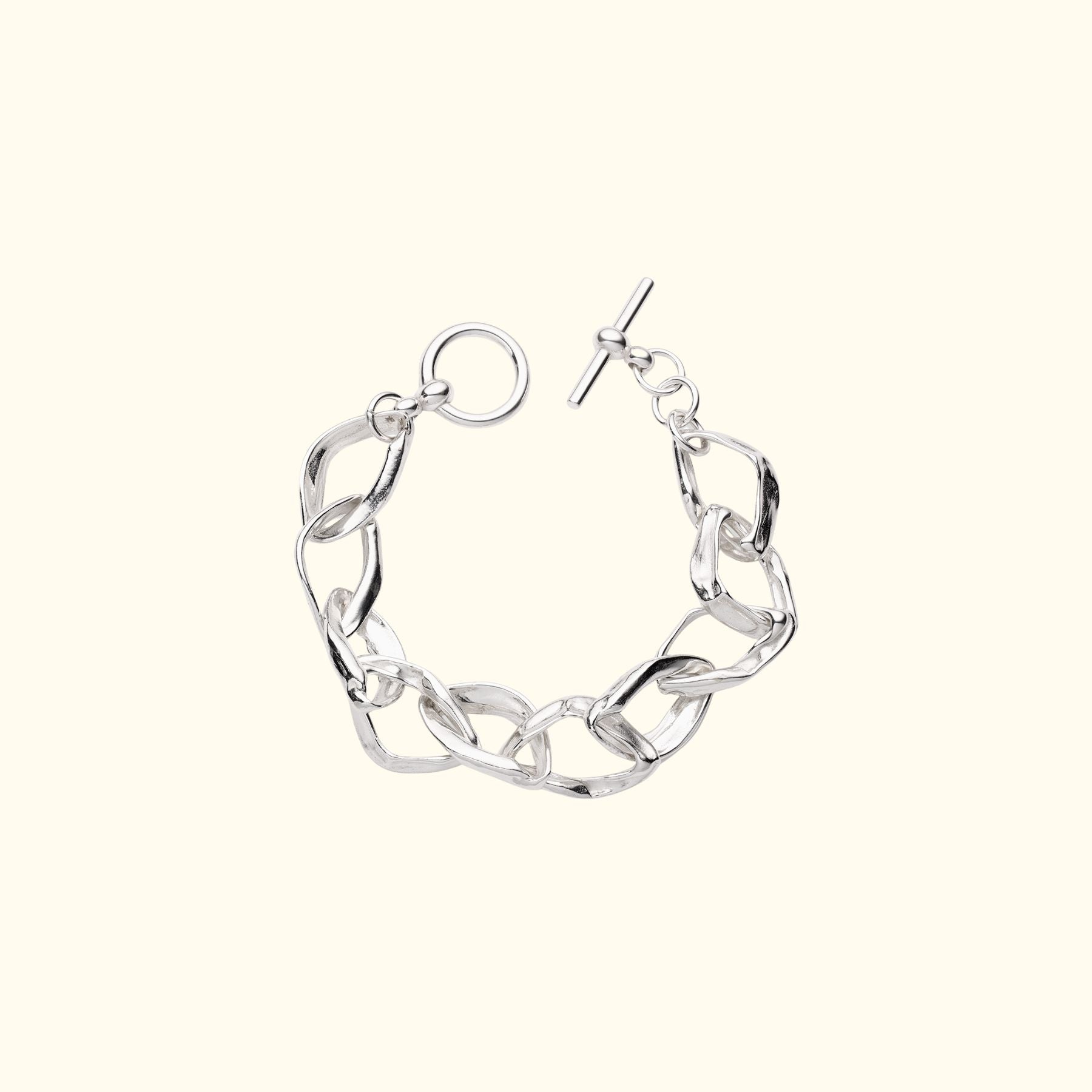 A silver chunky abstract chain link bracelet by Jessica Liu with a toggle clasp, displayed on a solid cream-colored background.