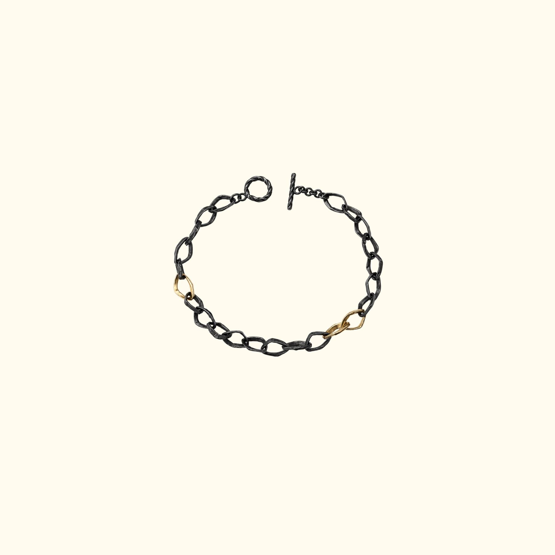 A delicate black oxidized chain bracelet by Jessica Liu with a toggle clasp and three small 18k gold accent links, displayed on a solid cream background.