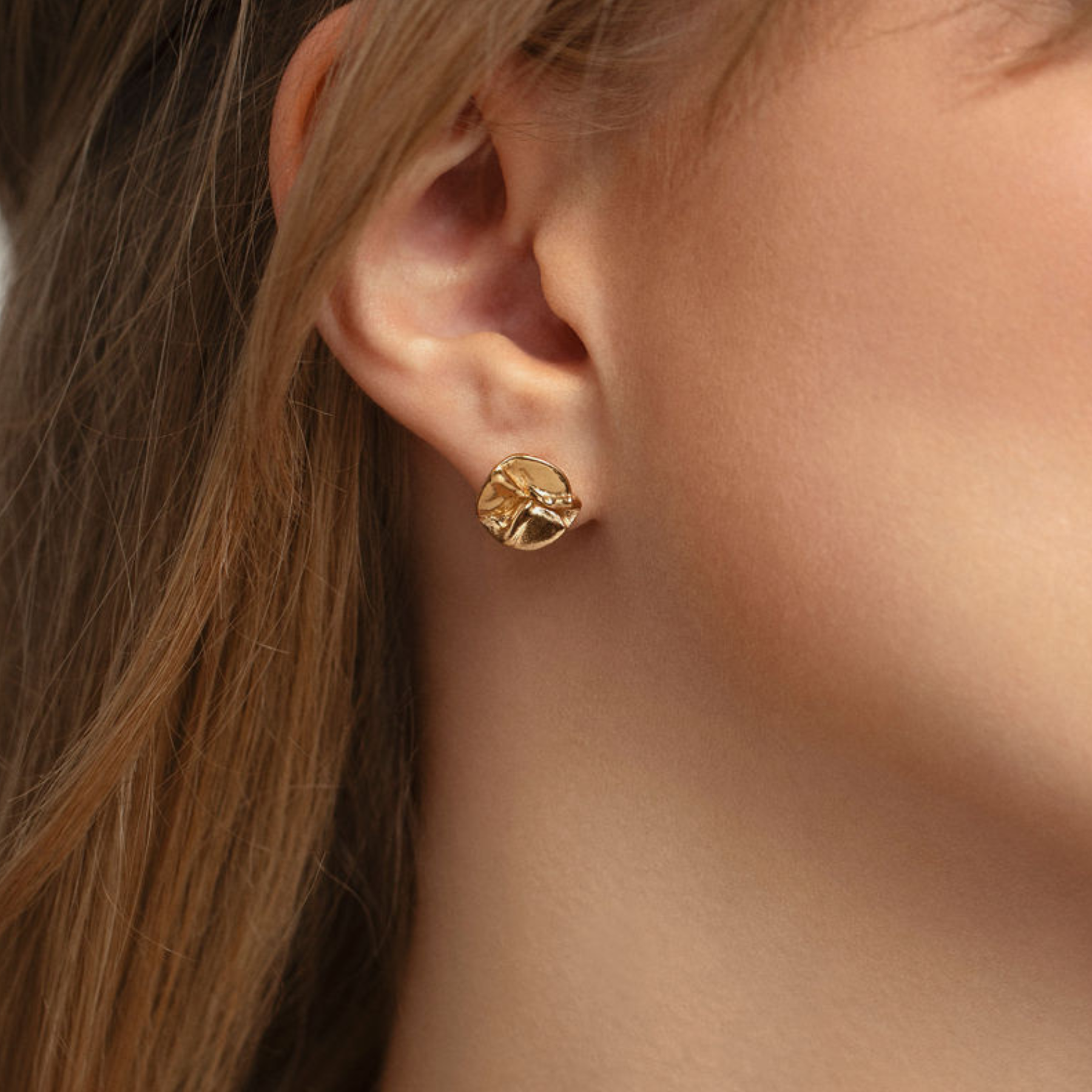 closeup of model wearing 14k gold small abstract lily pad stud earrings by jessica liu