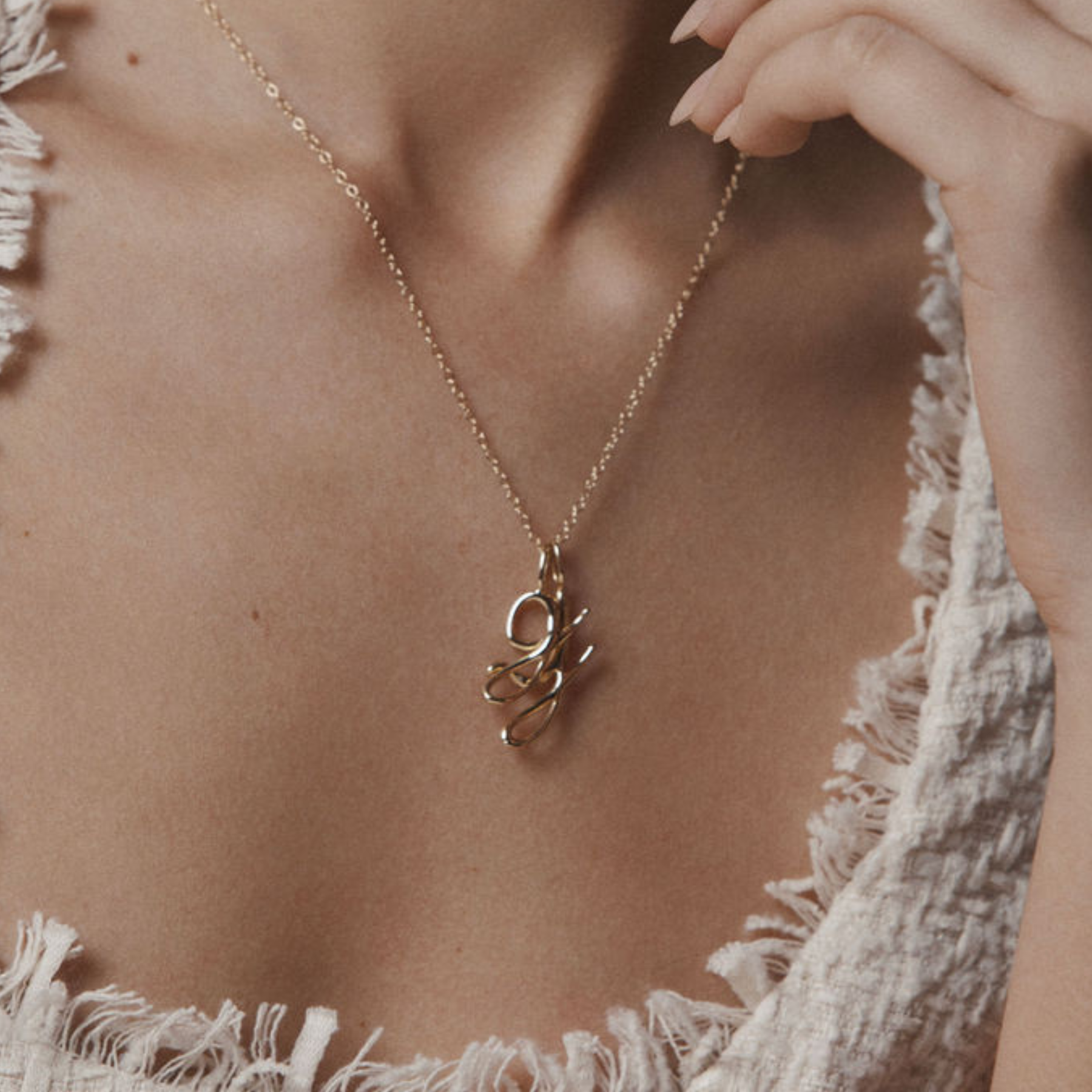 closeup shot of model wearing 14k gold letter g and j pendants on a delicate gold chain by jessica liu