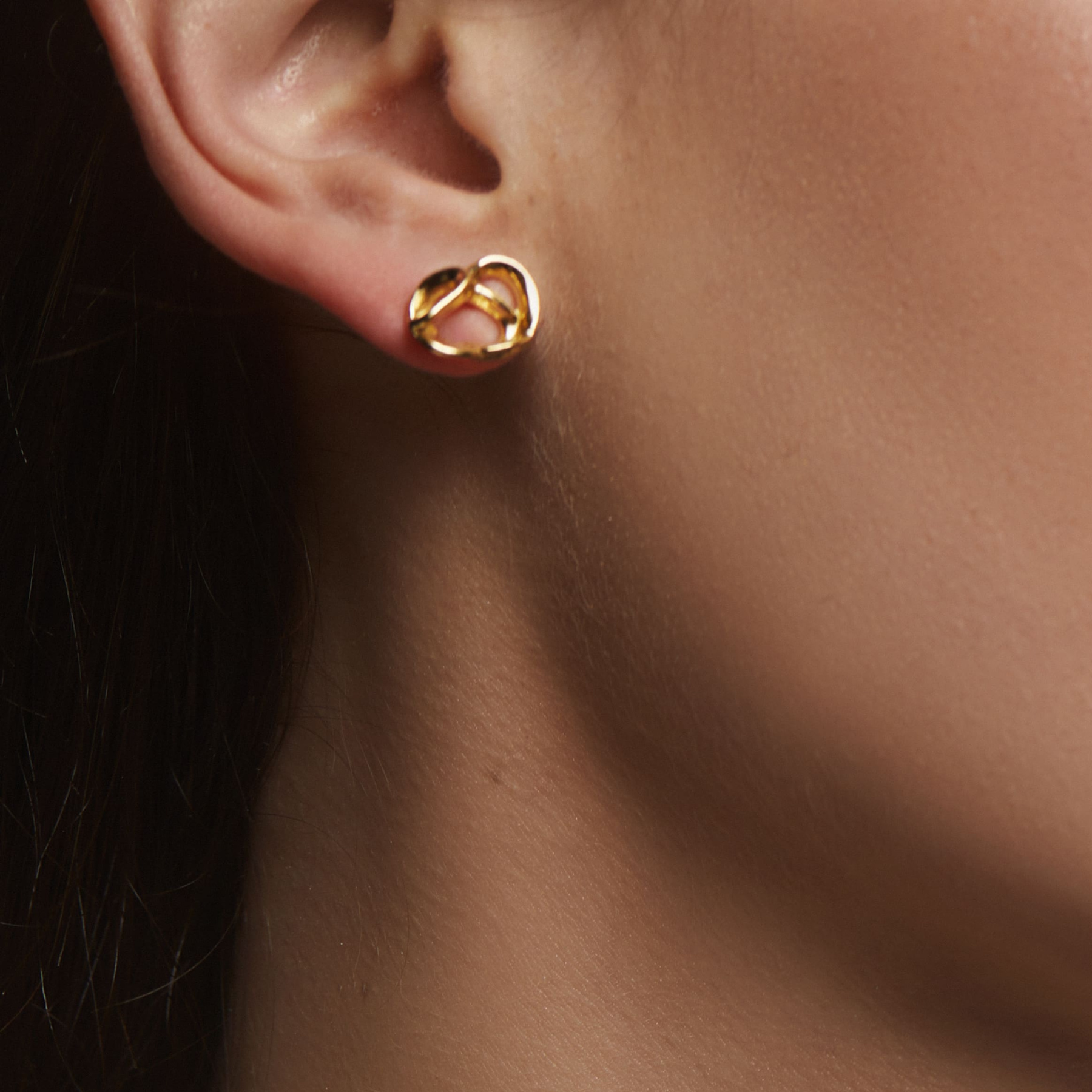 closeup shot of ear showing 14k gold abstract pretzel stud earring by jessica liu