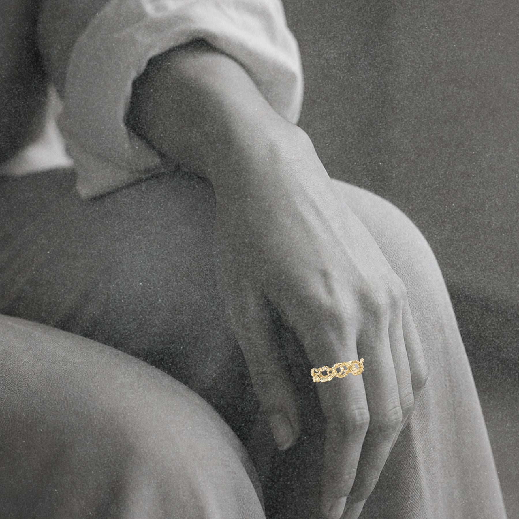 A close-up of a person's hand resting on their knee, wearing an organic gold chain ring by Jessica Liu.