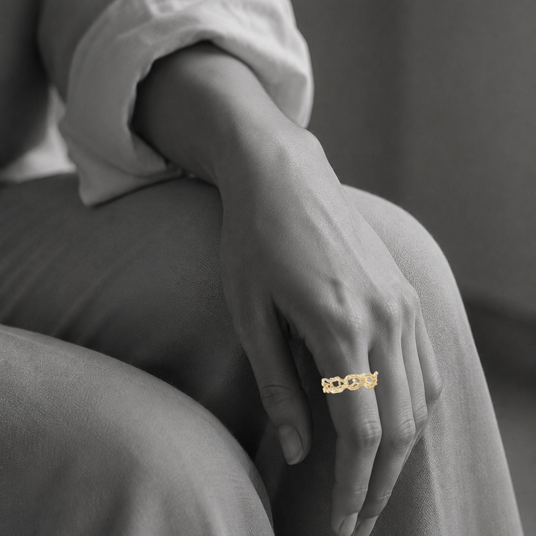 A close-up of a person's hand resting on their lap, wearing a delicate organic chain gold ring by Jessica Liu.