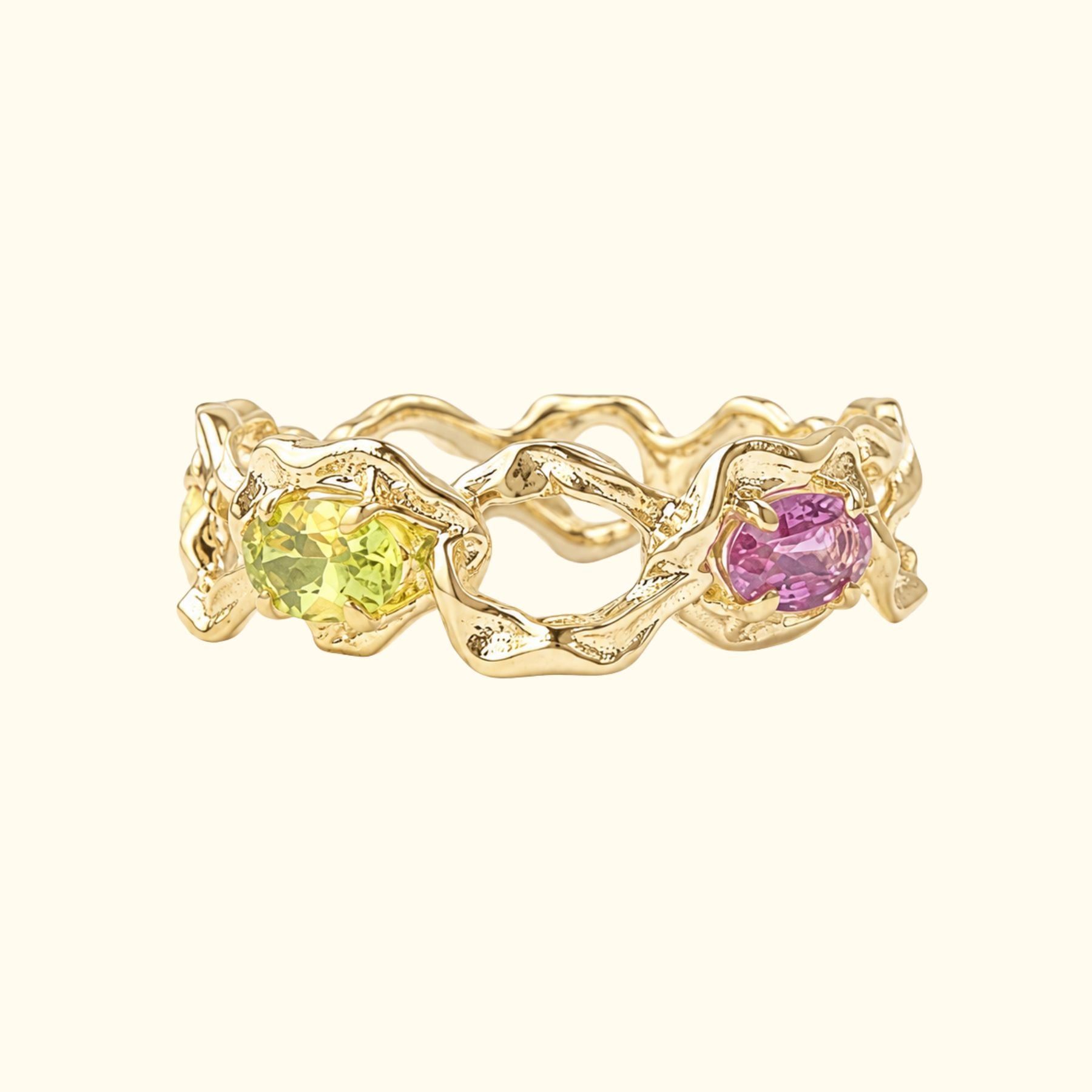 A gold ring by Jessica Liu with an organic, wavy textured band showing two oval gemstones, one yellow-green and one pink, set against a solid cream background.
