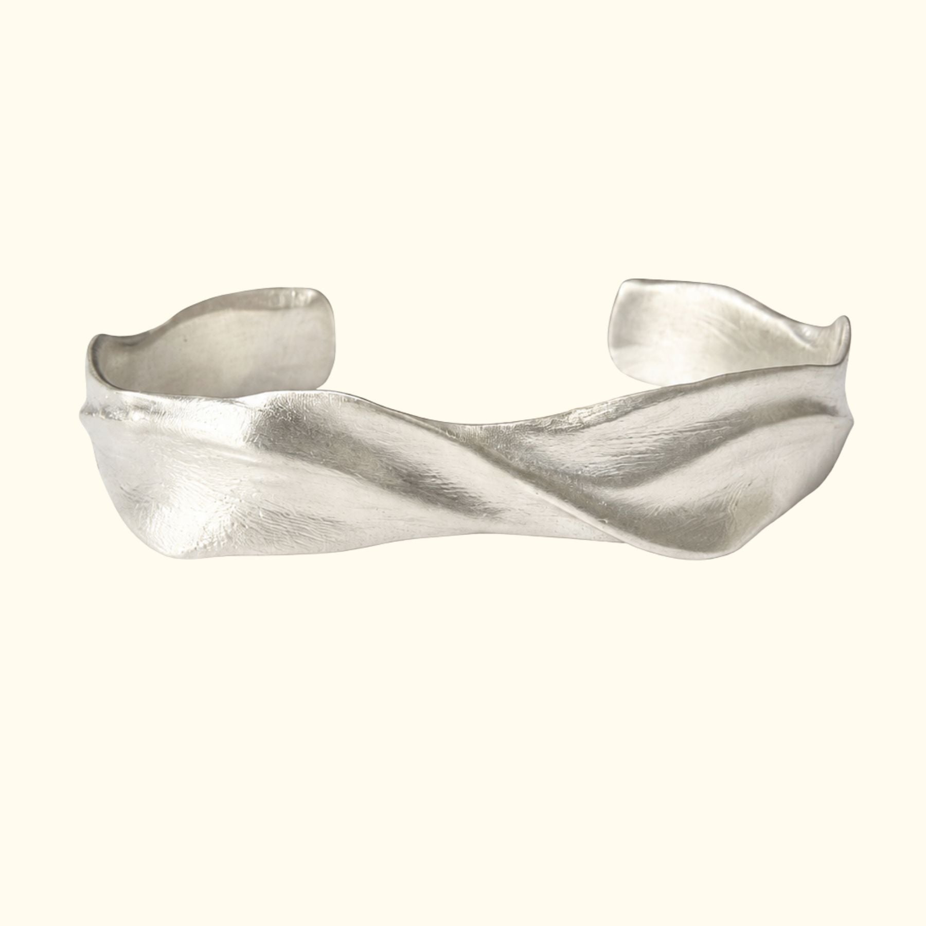 A sculptural silver cuff bracelet by Jessica Liu  with a twisted, organic wave design, shown against a solid cream background.