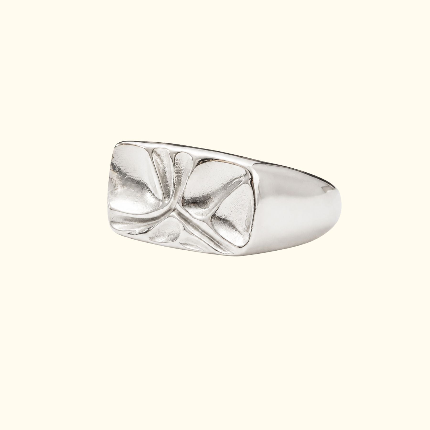 A silver signet ring by Jessica Liu with a textured, abstractly fluid pattern on the face, shown on a solid cream background.